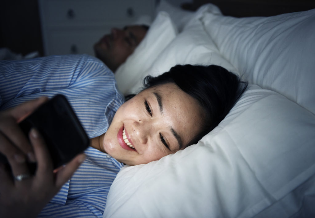 Asian woman using phone on a bed